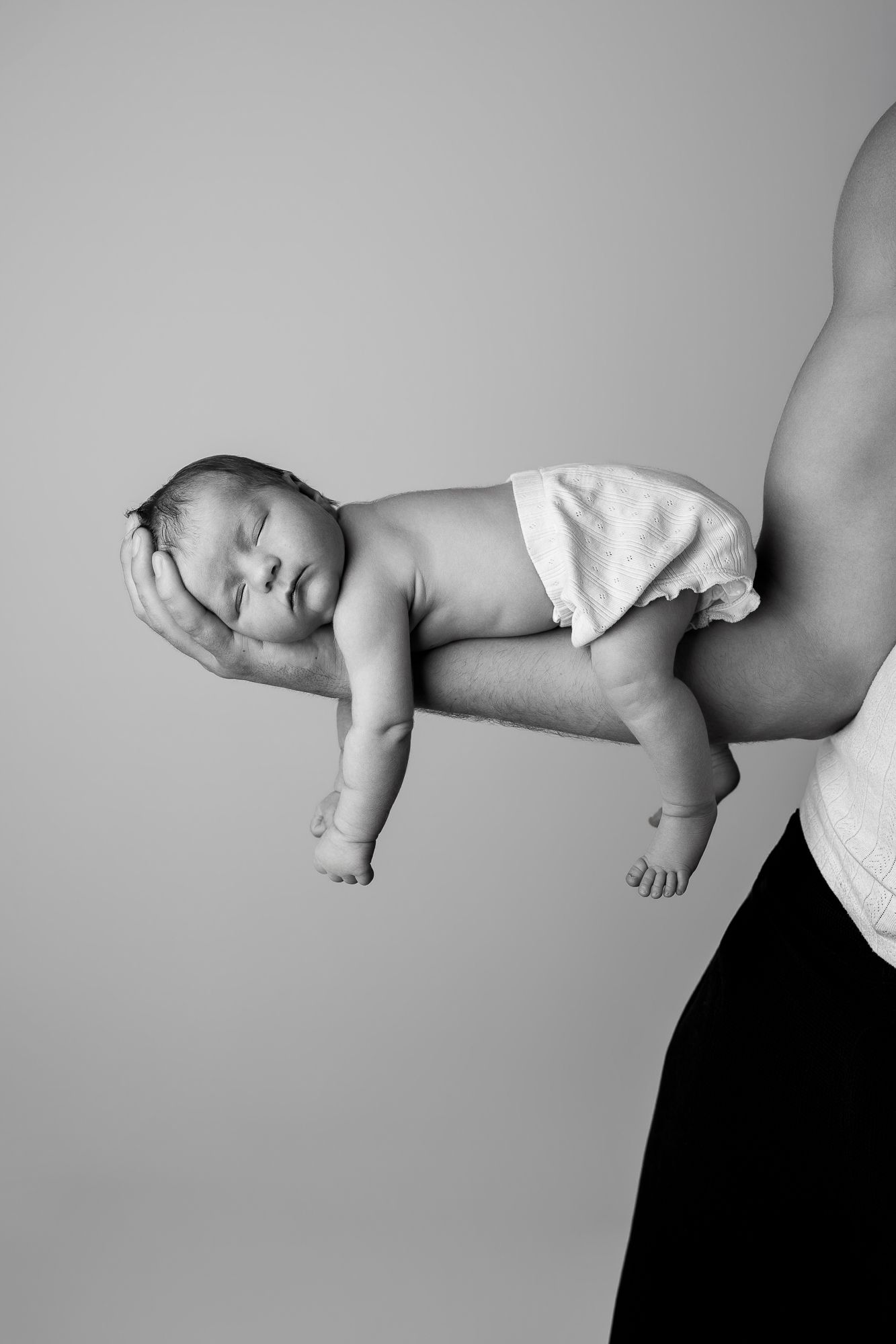 Black and white photo of a sleeping newborn baby held carefully on an adult's forearm in a diaper.
