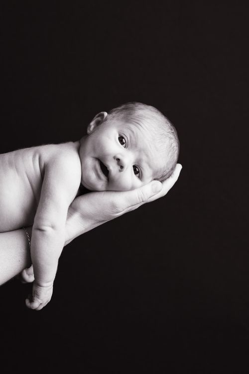 Black and white photo of a newborn baby resting on an adult's hand against a dark background.