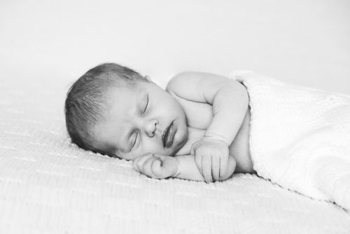 Black and white photo of a peaceful sleeping newborn baby lying on a soft white blanket.