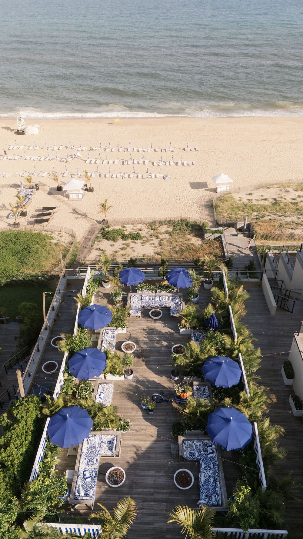 Aerial view of beachfront venue with blue umbrellas, wood deck, and sandy Atlantic Ocean shoreline.