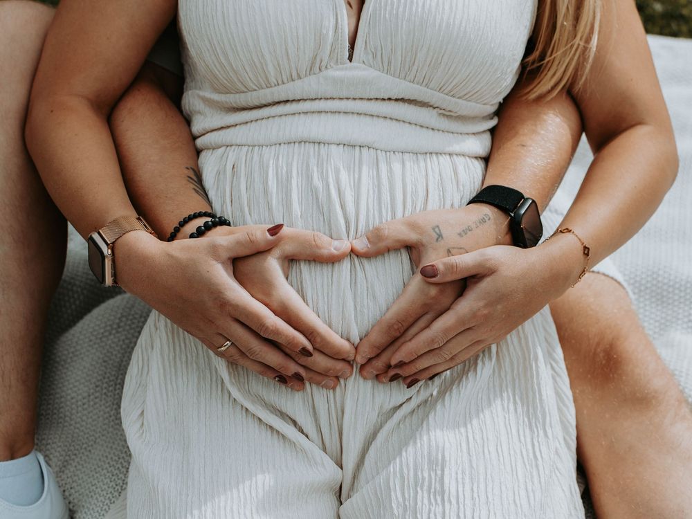 Couple forming heart shape with hands on pregnant belly.