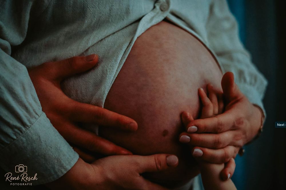 Close-up of pregnant belly with multiple hands gently cradling it, capturing a tender family maternity moment.