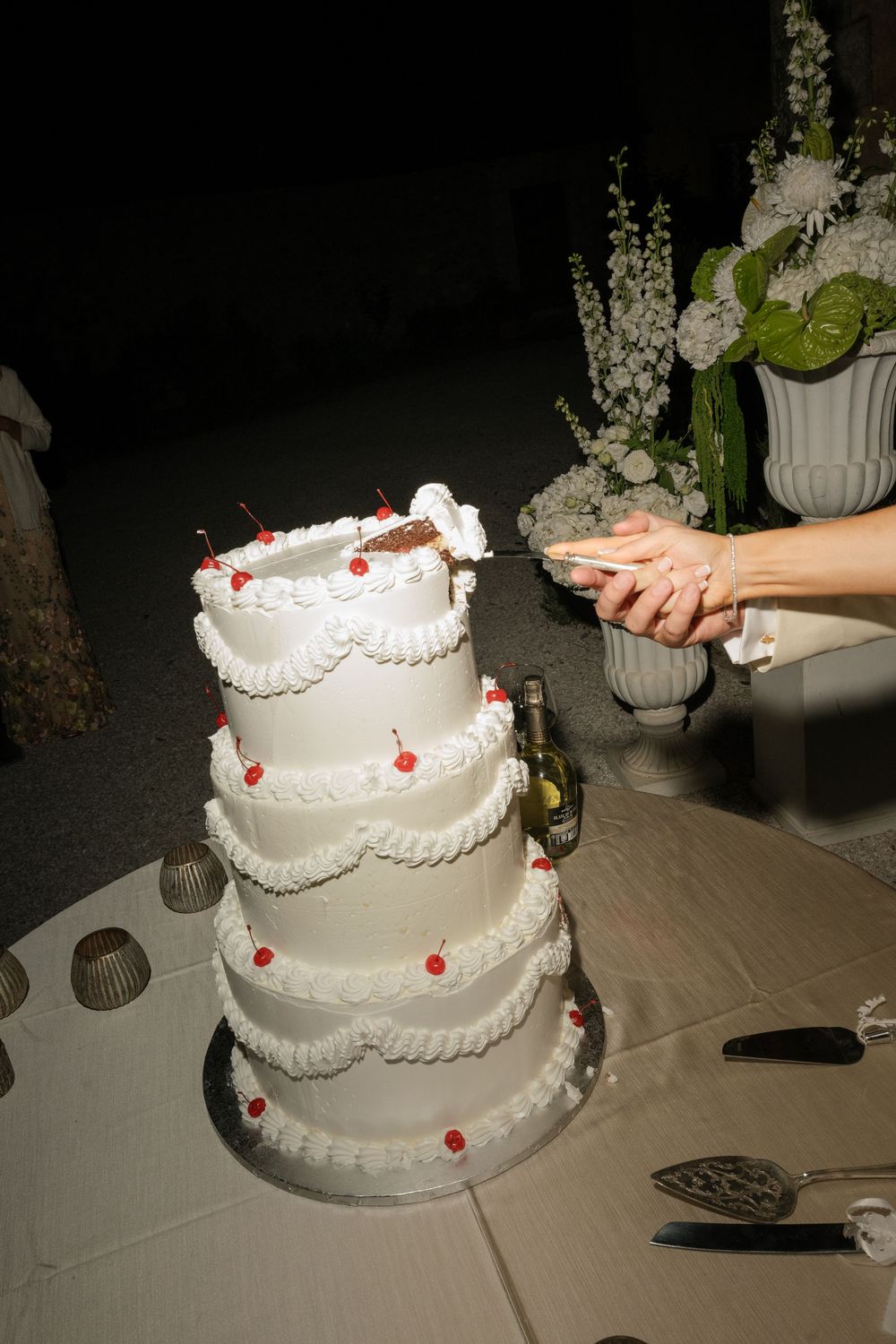 Bride and groom cutting a four-tier white wedding cake decorated with red cherries at a wedding reception.