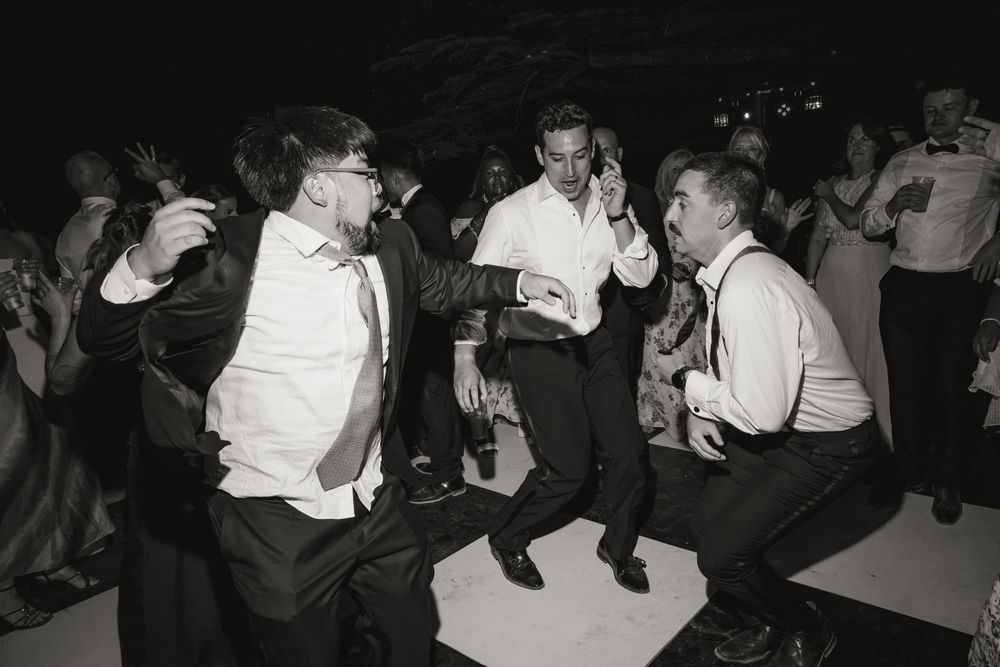 Black and white photo of men dancing energetically at a wedding reception on a dance floor.