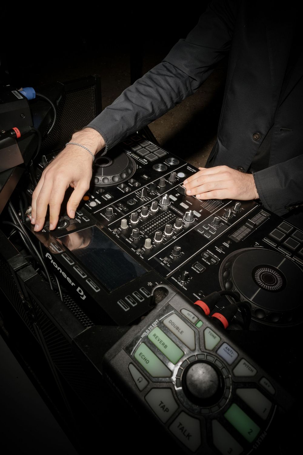 DJ hands operating a Pioneer DJ mixer and turntable controller at a nightclub event.