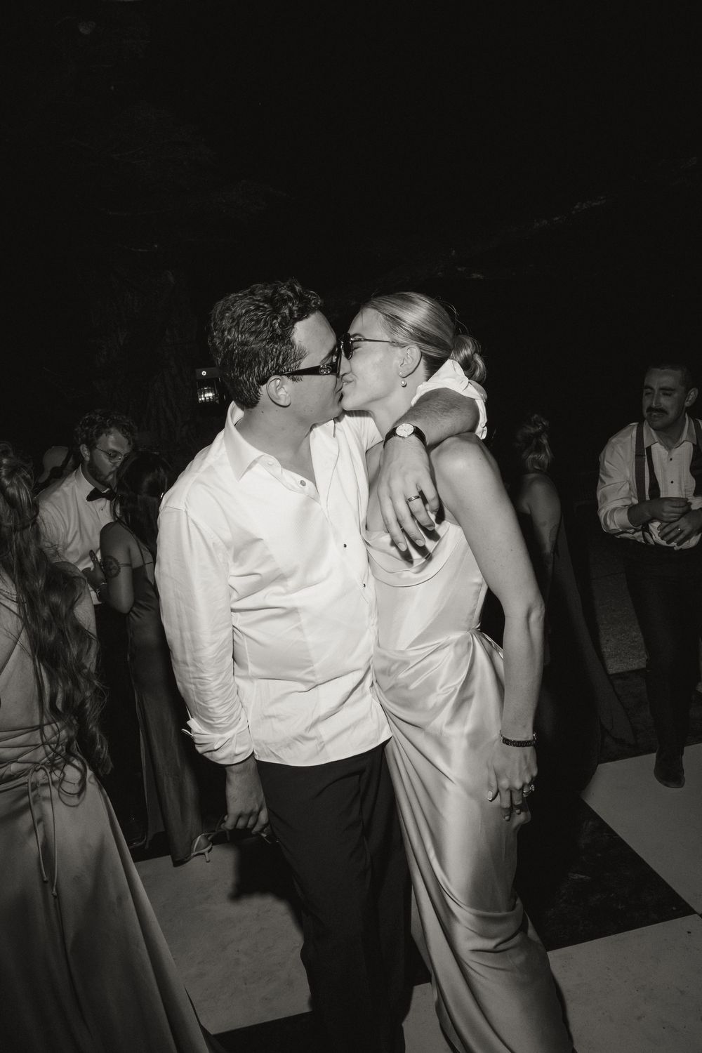 Black and white photo of a couple sharing a kiss while dancing at a wedding reception.