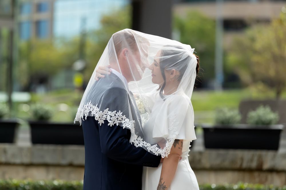 Bride and groom share an intimate moment under a lace-trimmed wedding veil outdoors on their wedding day.