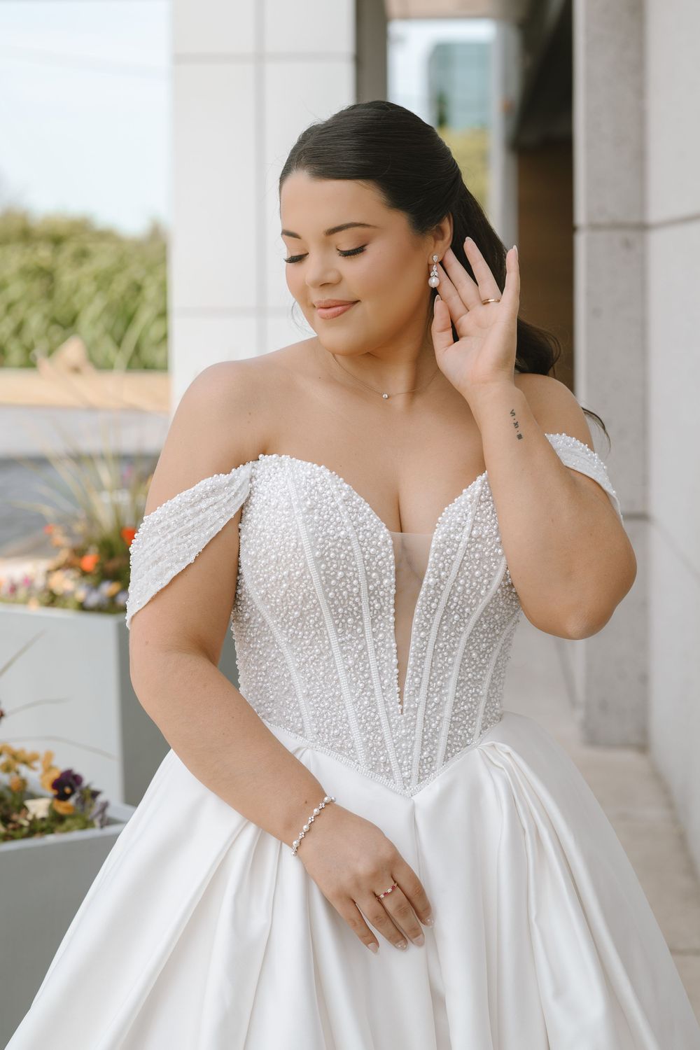 Plus-size bride wearing a pearl-embellished off-shoulder ball gown wedding dress with corset bodice.
