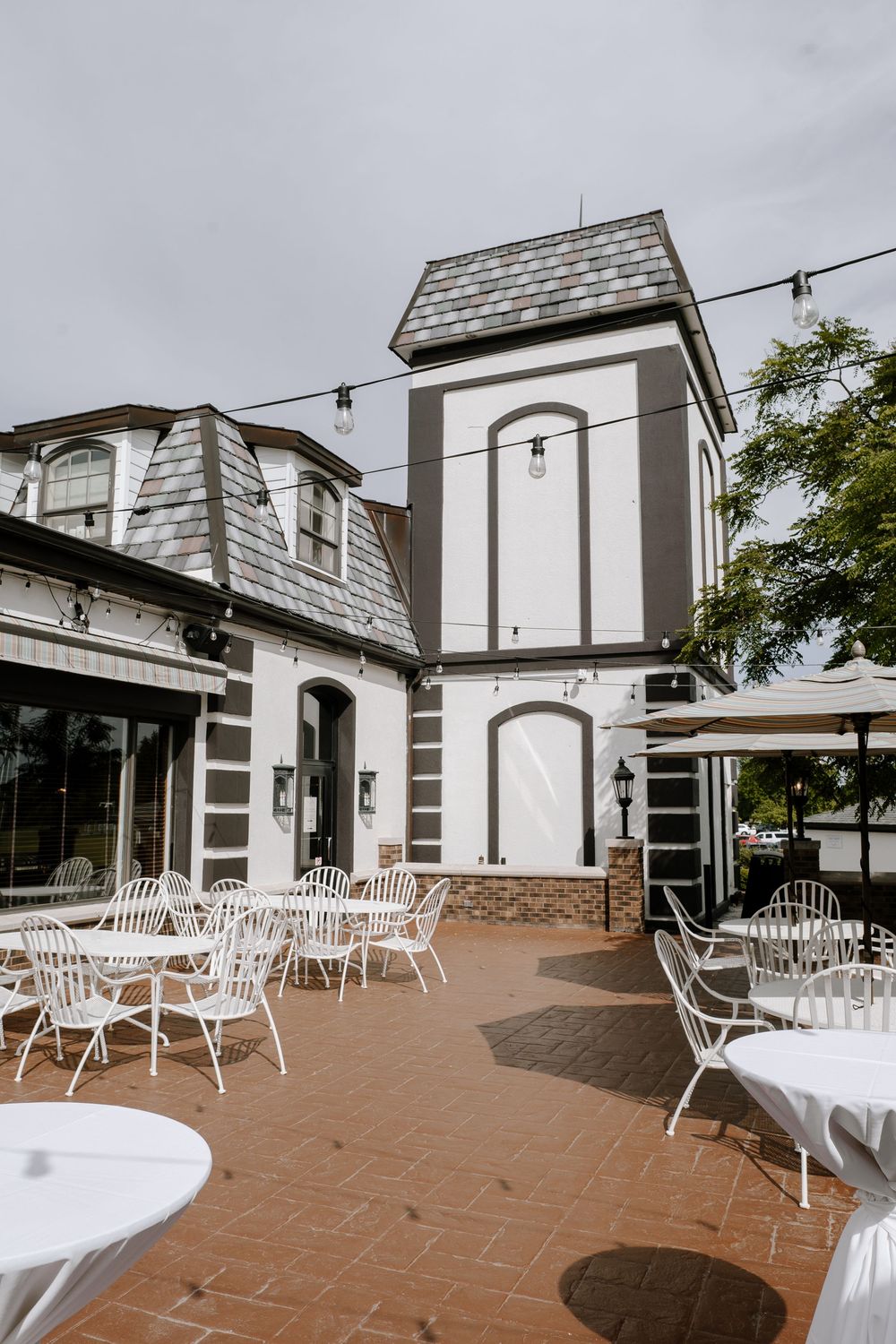 Elegant outdoor patio with white bistro chairs and tables at a wedding venue with string lights.