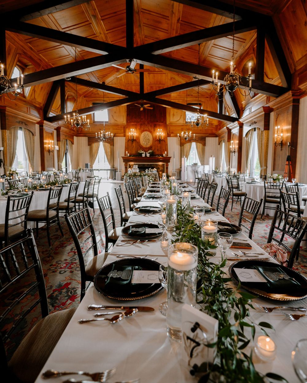 Stunning wedding reception hall with wooden cathedral ceiling, long tables, greenery, and candlelight.