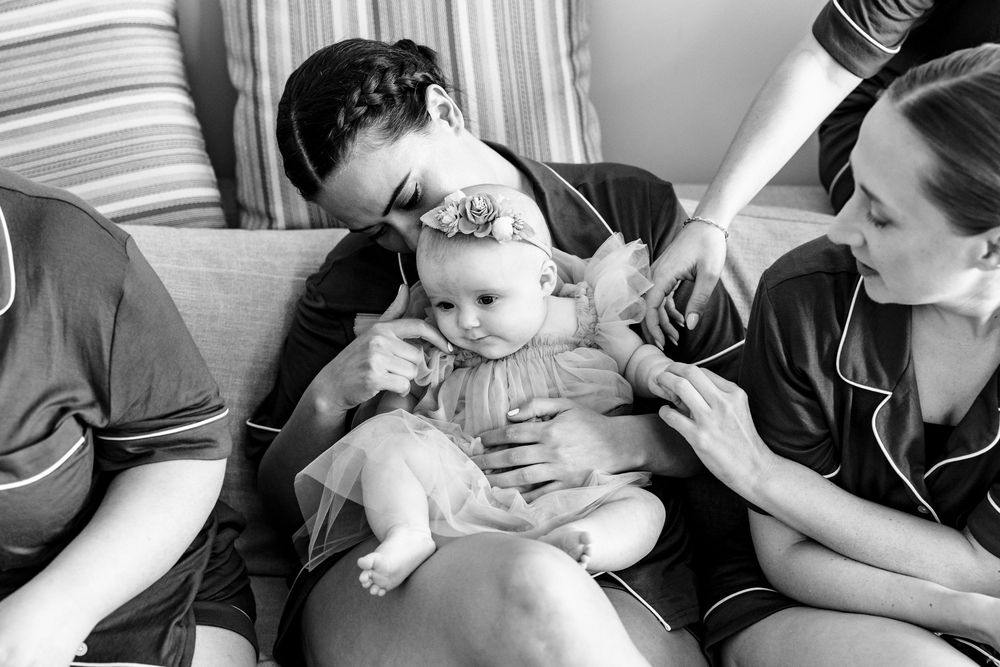 Black and white photo of a mother kissing her baby girl while a bridesmaid assists during wedding preparations.