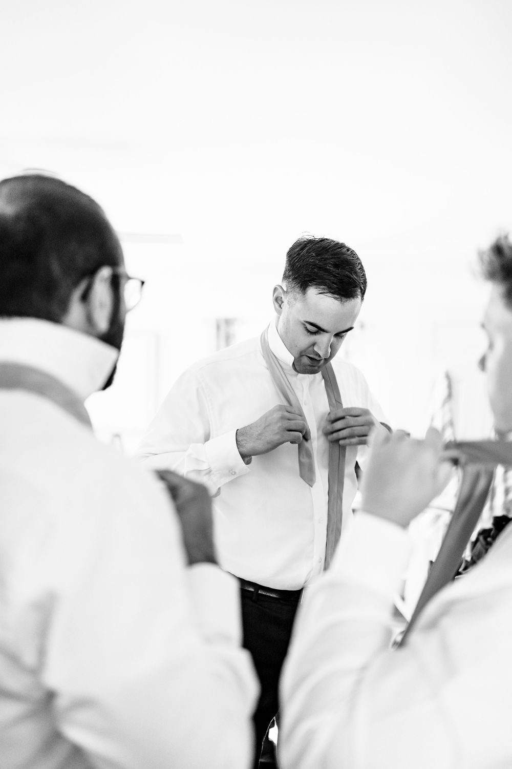 Groom adjusting his tie while getting ready with groomsmen in black and white wedding preparation photo.