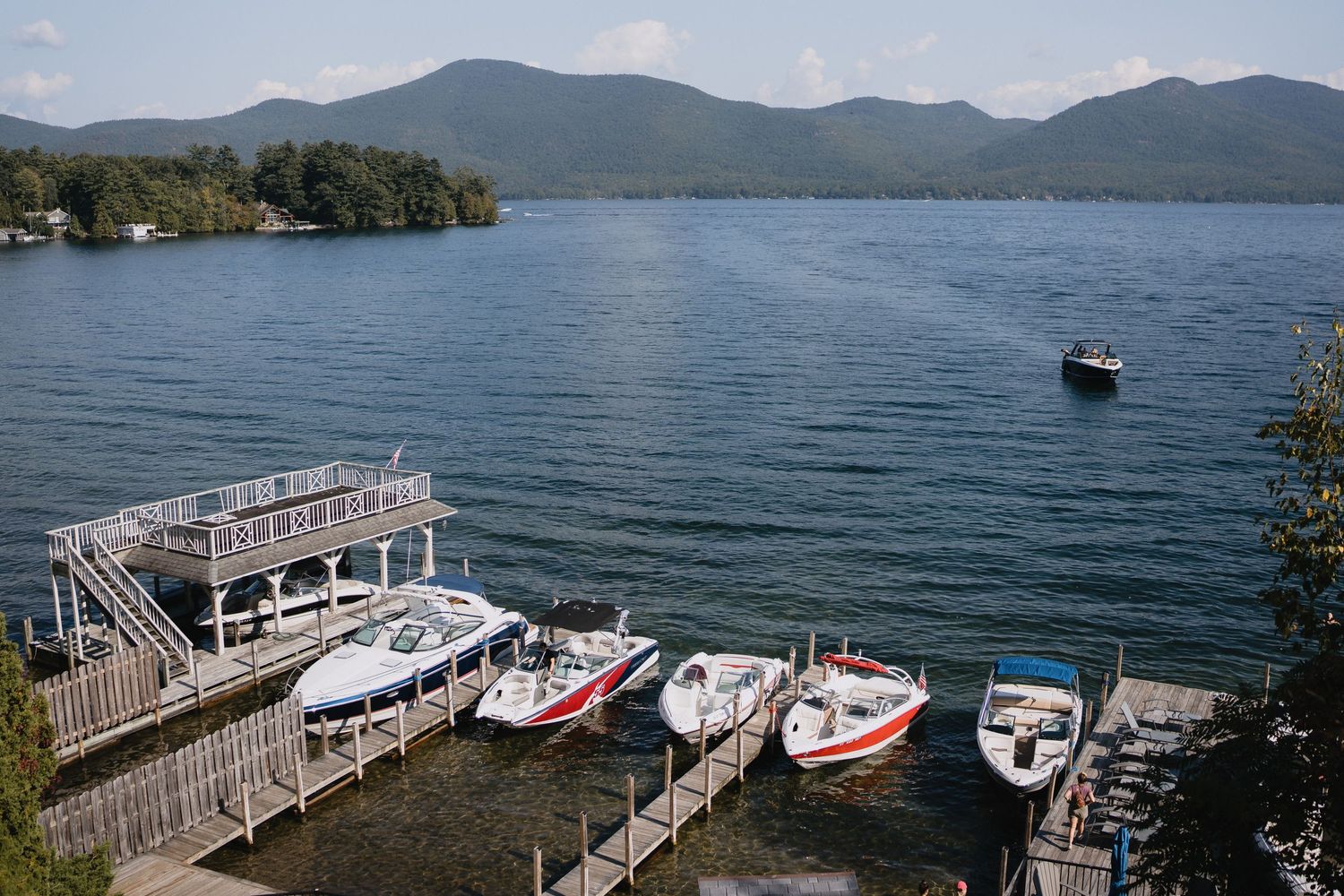 Several colorful boats docked at a wooden pier on a calm mountain lake with scenic peaks in the background.