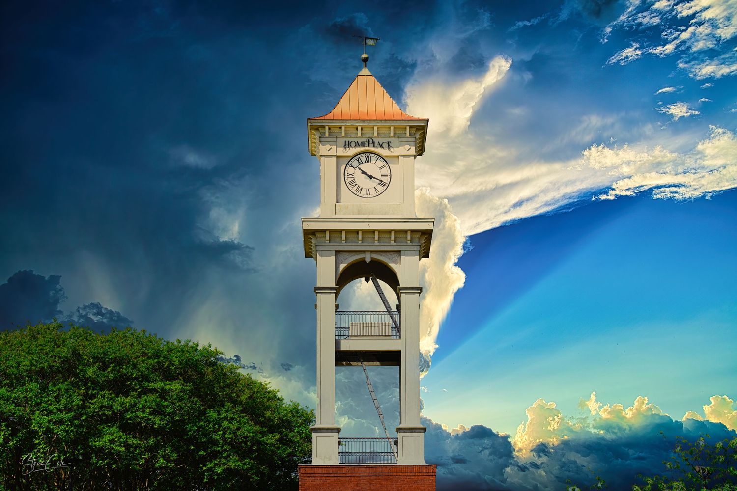 Historic clock tower in Prattville, Alabama, standing tall against a dramatic sky with storm clouds, photo by Steve Cole Photography.
