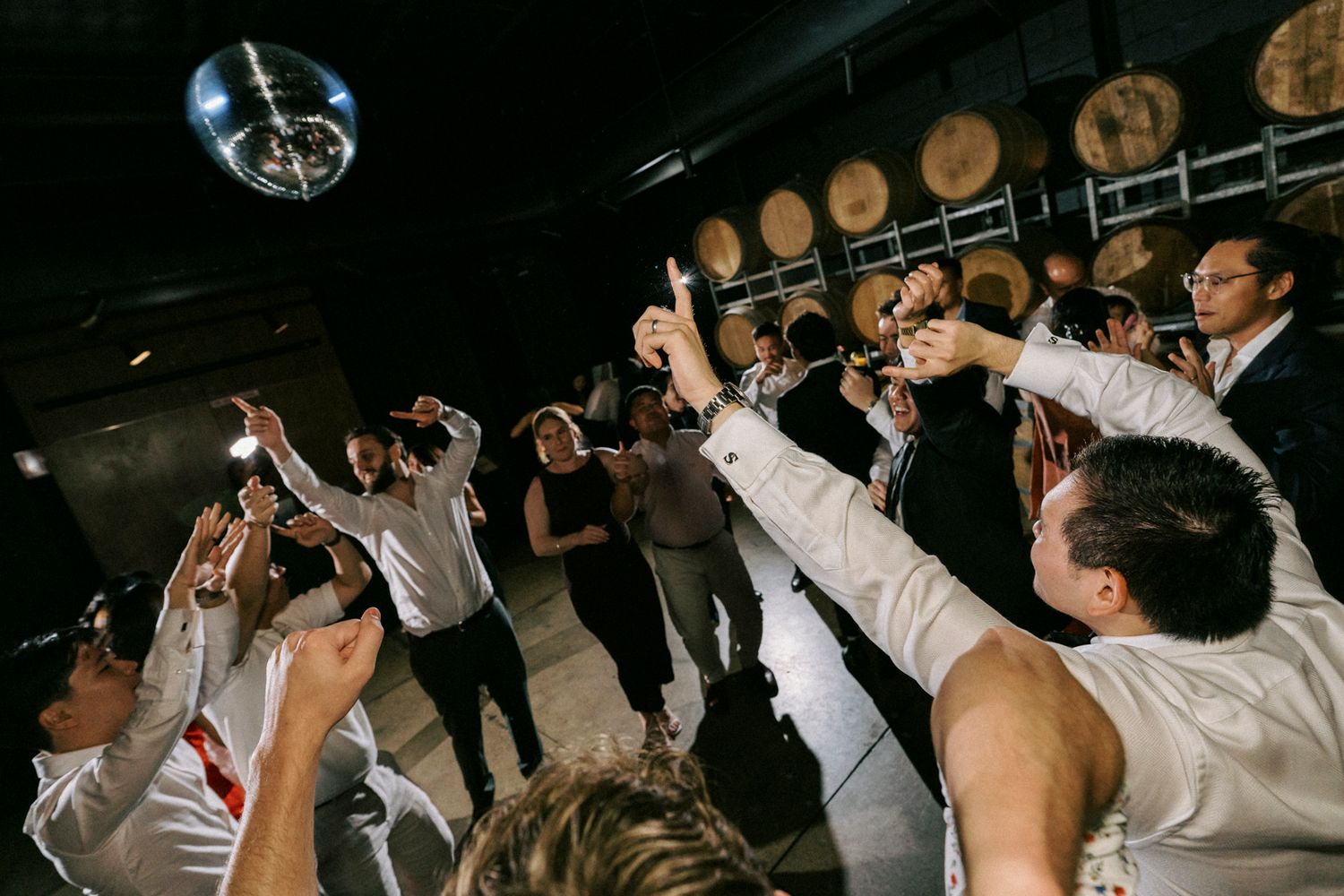 Guests raising glasses in a toast at a lively party with disco ball and wooden barrels in background.the bethnal. Newstead Brisbane