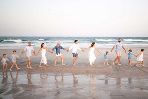 Large family holding hands walking along a sandy beach in matching white and blue outfits near ocean waves.