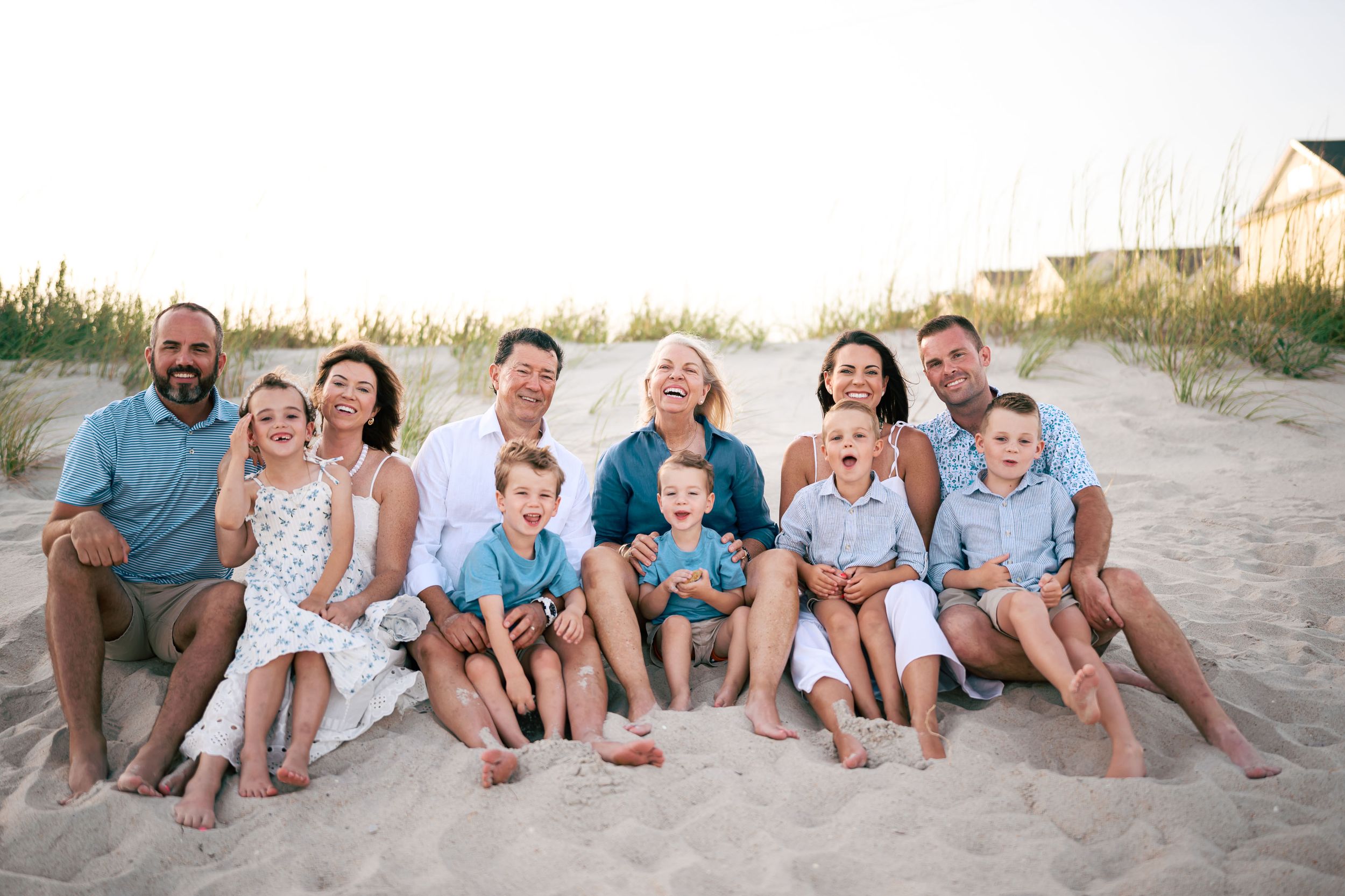Large family group smiling together on sandy beach during golden hour photo session.