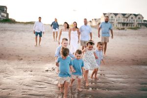Family with children walking along shoreline during beach photo session at sunset.