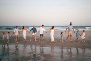 Large family holding hands walking along a beach at sunset, dressed in white and blue outfits.