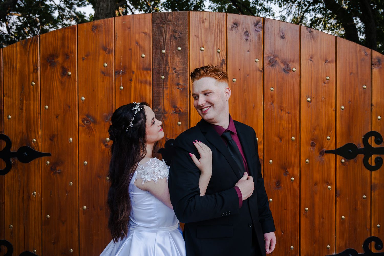 Bride and groom share first kiss at wedding ceremony with pink floral arch backdrop and barrel decorations.
