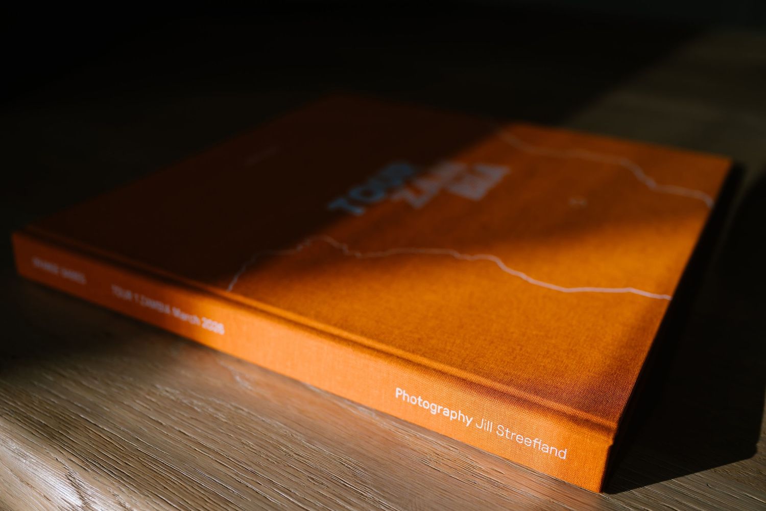 Orange hardcover photography book lying flat on a wooden surface, showcasing its spine and textured cover design.