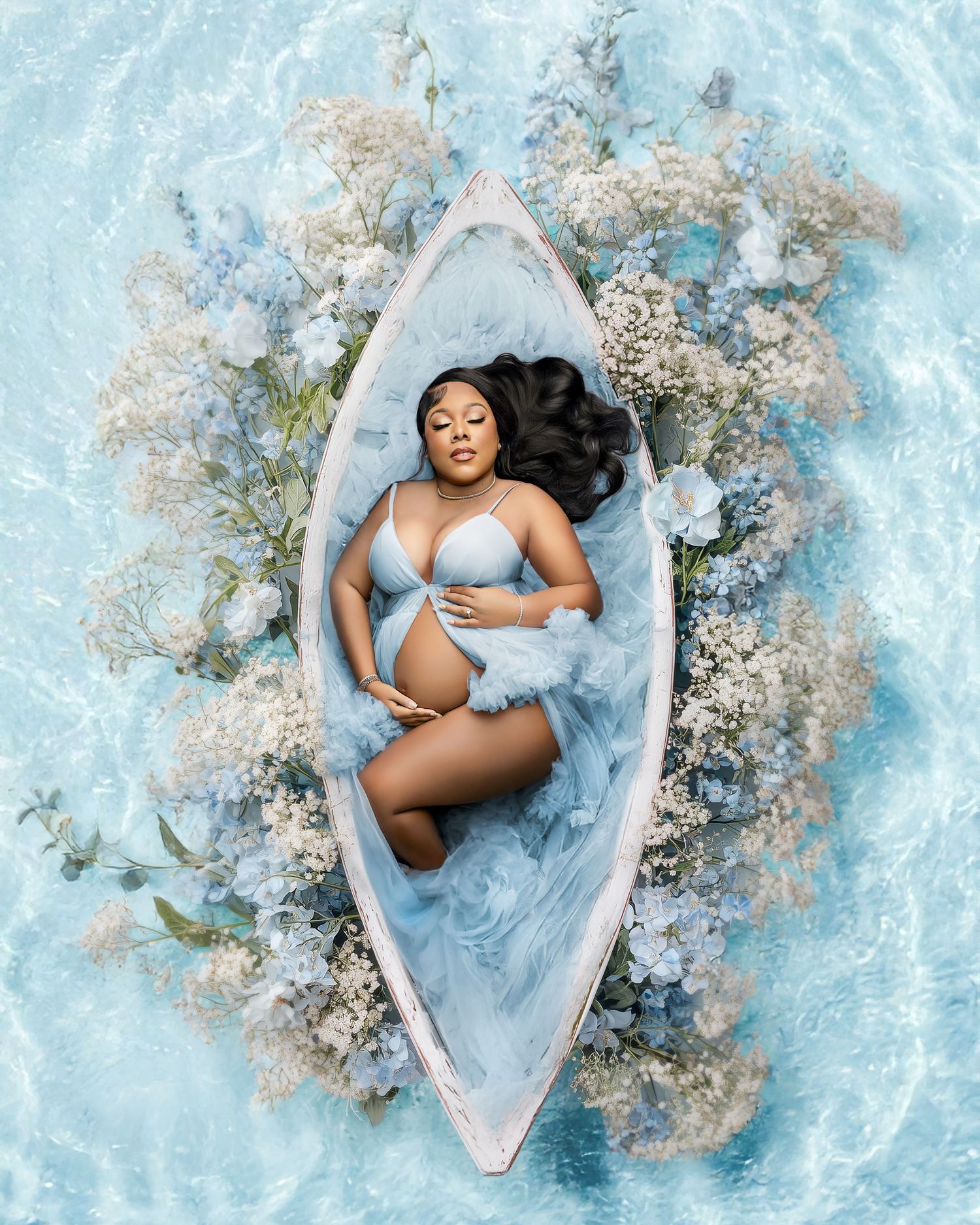 Pregnant woman in blue lingerie lying in a floral-decorated white boat surrounded by blue water.