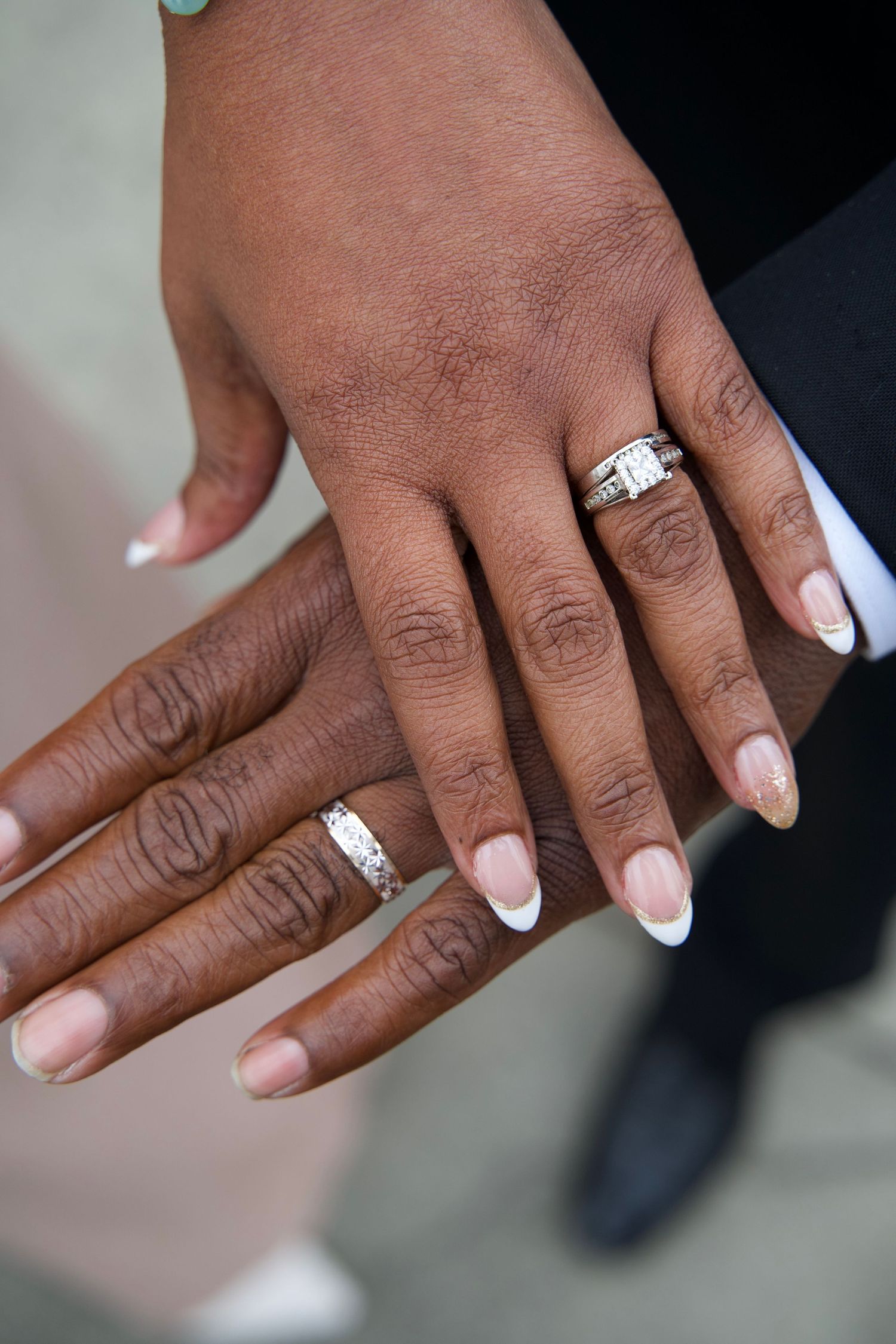 Close-up of newlywed couple displaying wedding rings, bride wearing diamond engagement ring with French manicure.