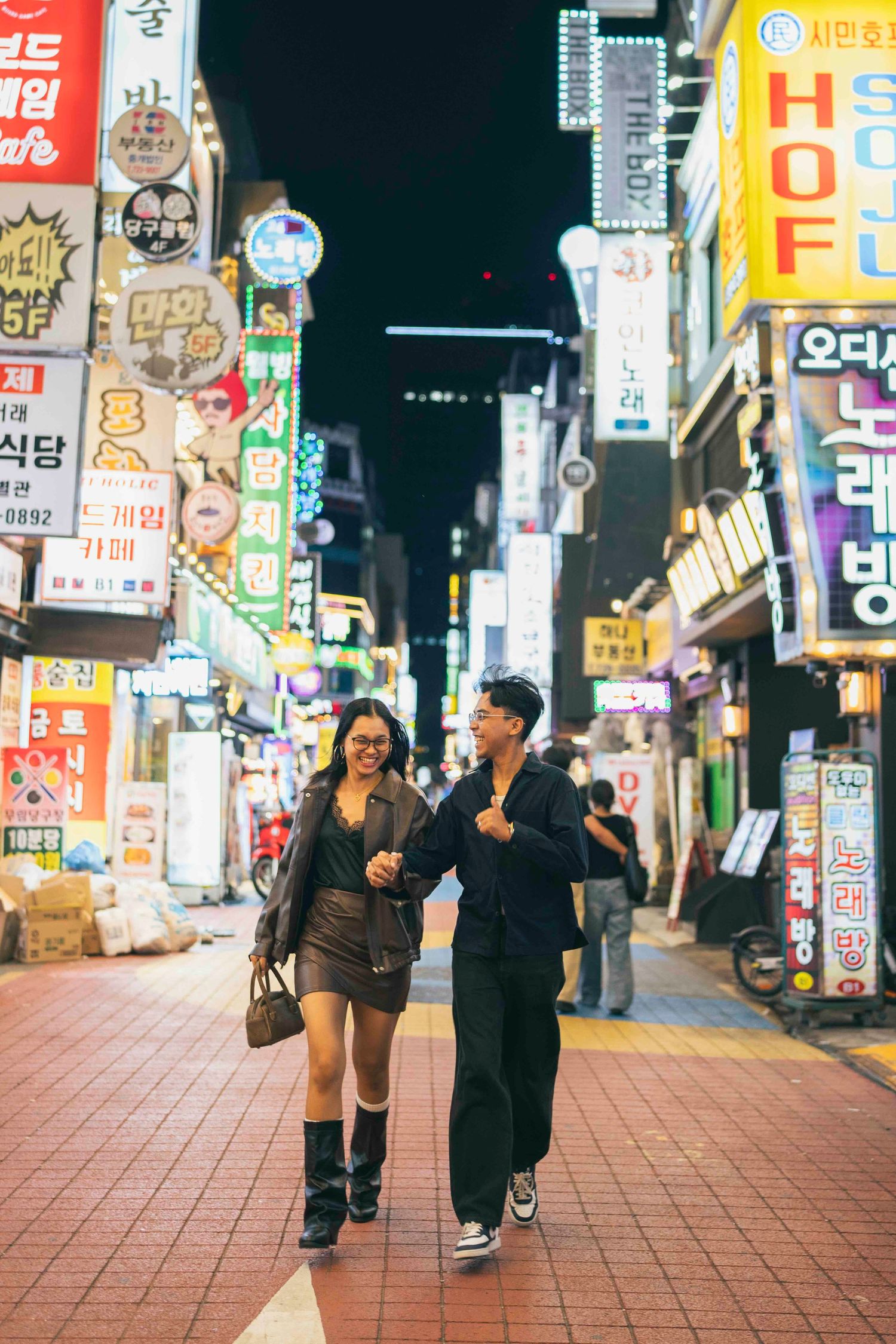 Couple walking together at night in a vibrant Seoul street filled with colorful Korean neon signs and busy storefronts.