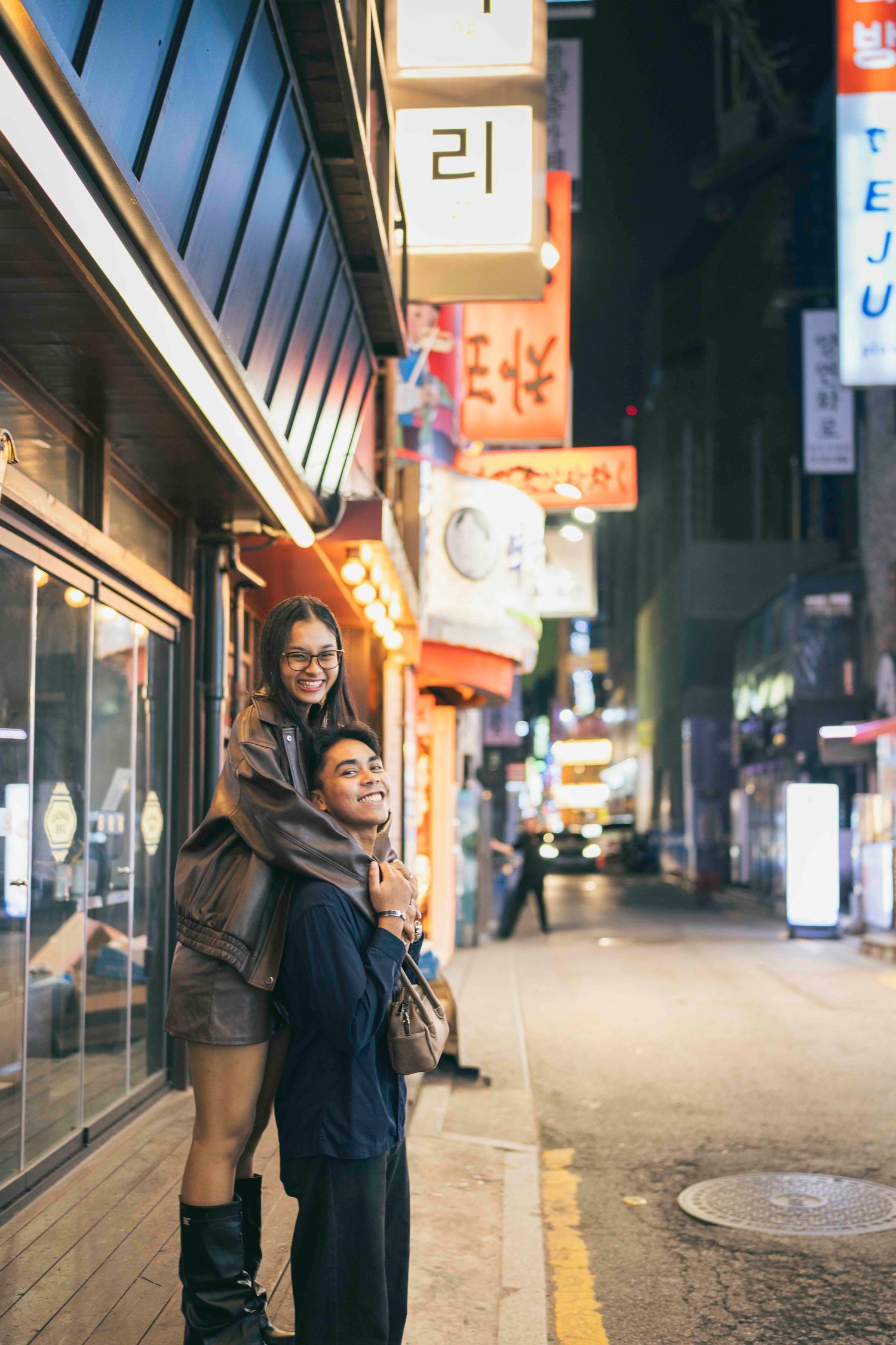 Couple posing on a vibrant Korean street at night, surrounded by colorful neon signs and city lights.
