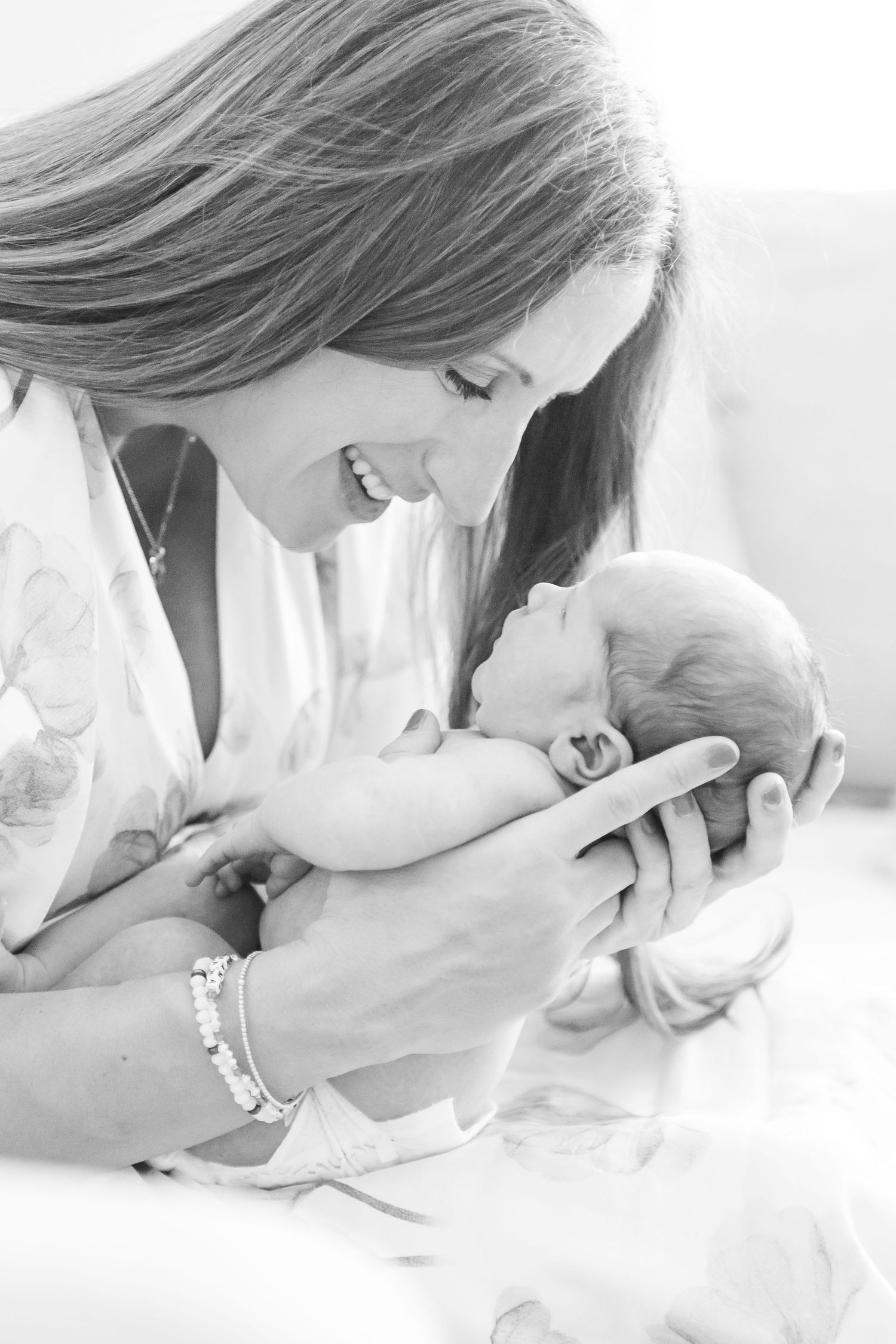 Black and white photo of smiling mother tenderly holding and gazing at her newborn baby.