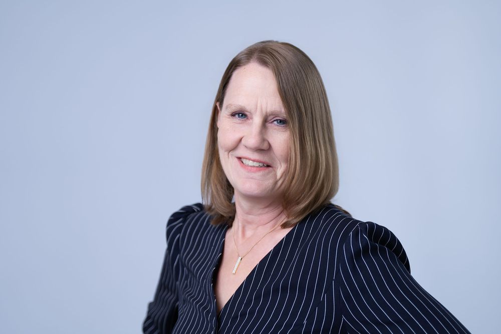 Smiling middle-aged woman with blonde hair in striped blazer poses for professional headshot.