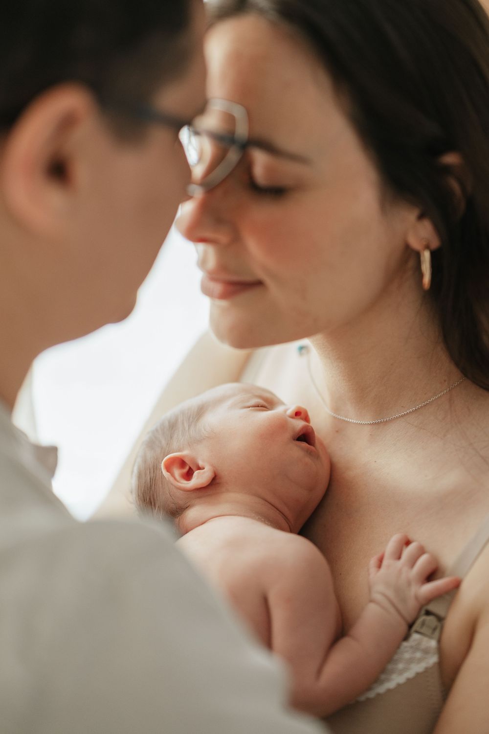 Parents tenderly holding their sleeping newborn baby close, sharing an intimate family moment.