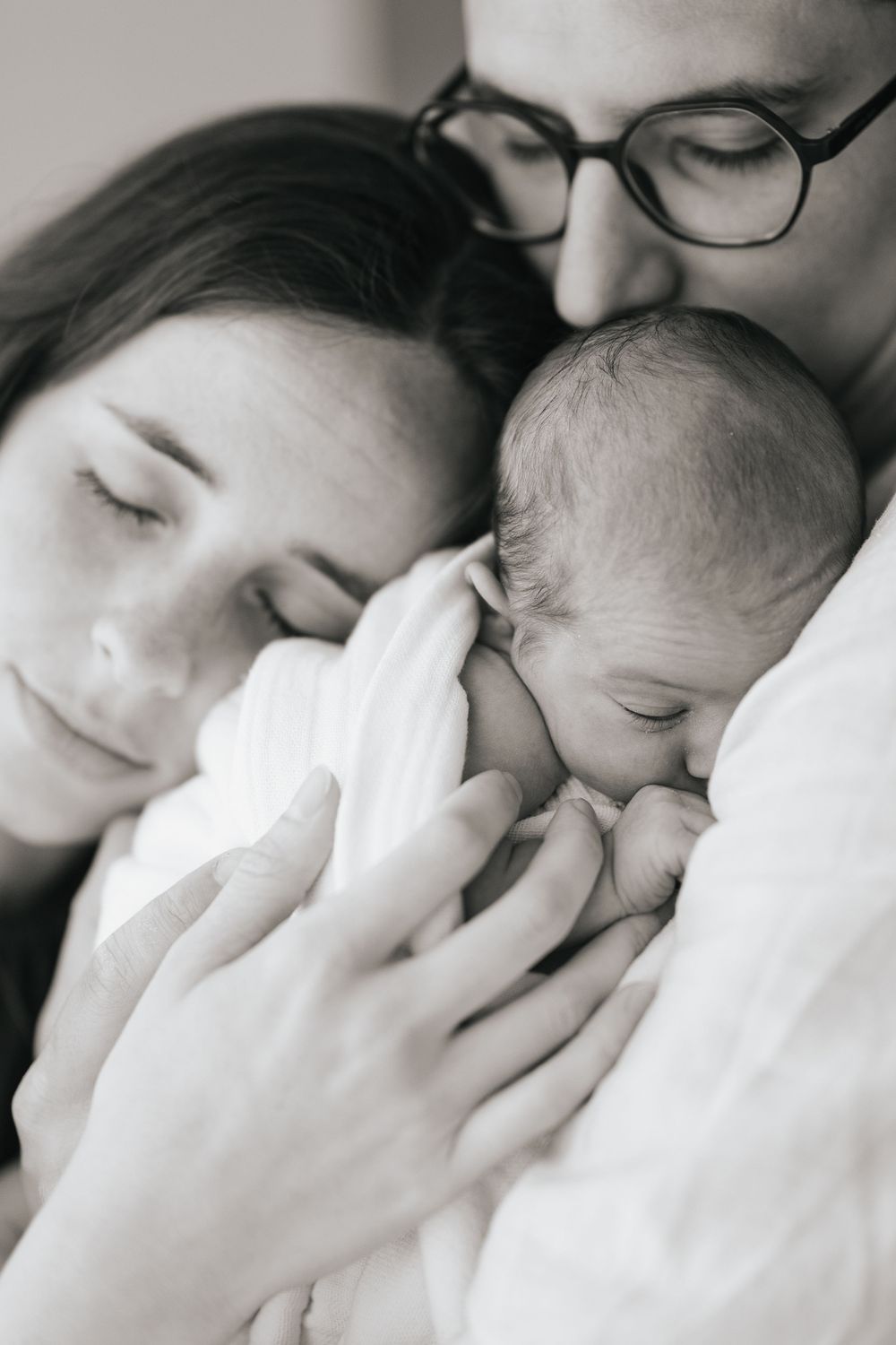 Black and white photo of new parents tenderly cradling their sleeping newborn baby together.