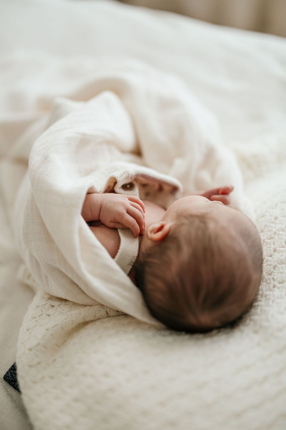 Newborn baby wrapped in a soft white blanket lying on a white textured surface, peaceful and serene.