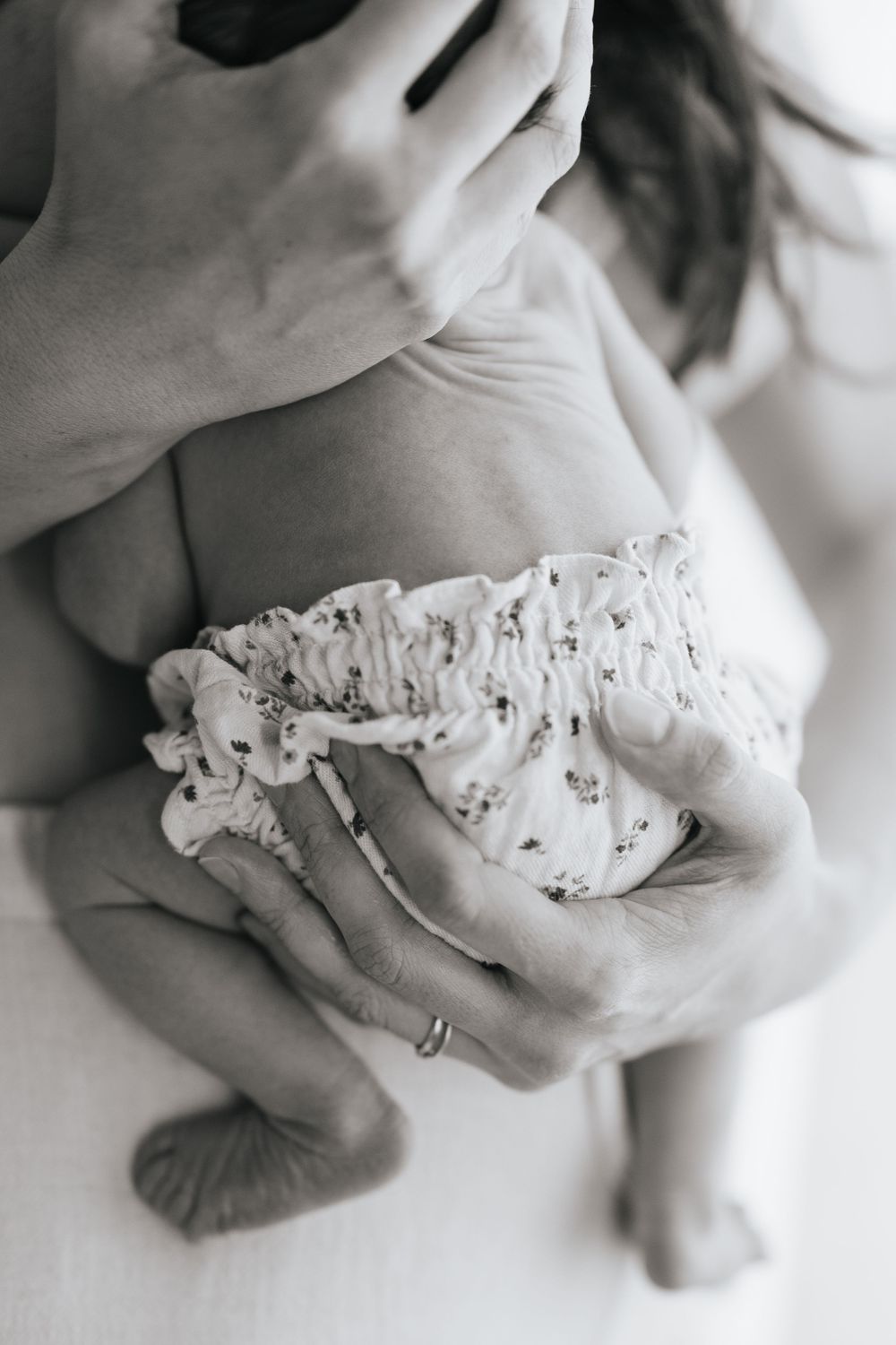 Black and white photo of a parent cradling a newborn baby wearing a floral diaper cover, close-up shot.