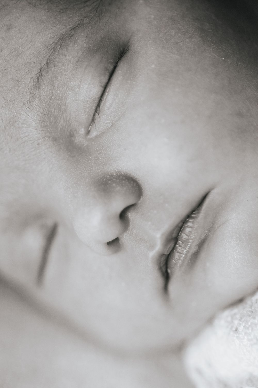 Close-up black and white portrait of a peaceful sleeping newborn baby's face.