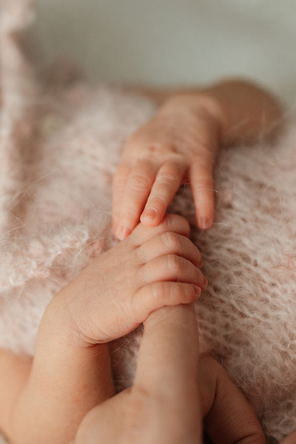 Close-up of a newborn baby's tiny hands resting on a soft pink fluffy blanket.