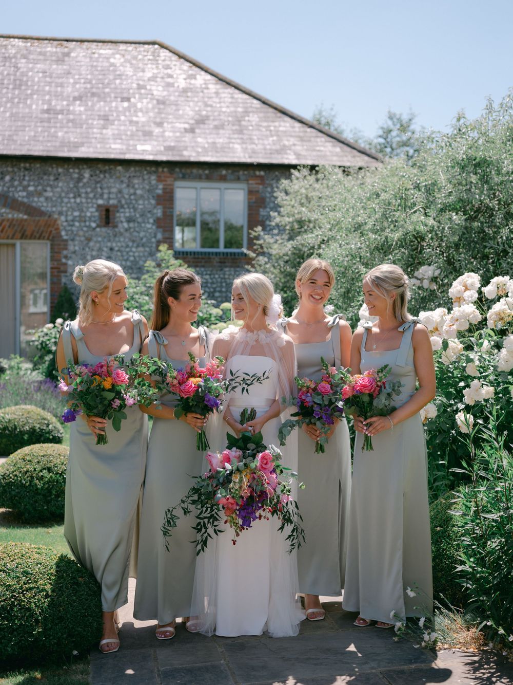 Wedding party posing with colorful bouquets against stone building backdrop at Farbridge.