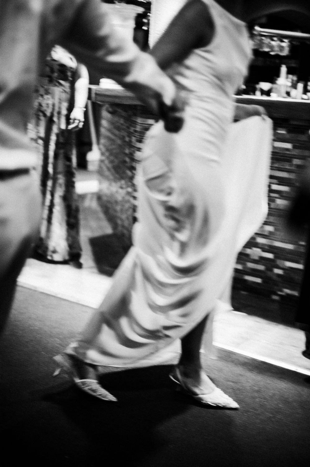Blurred black and white photo of a woman in a flowing gown dancing energetically at an elegant event.