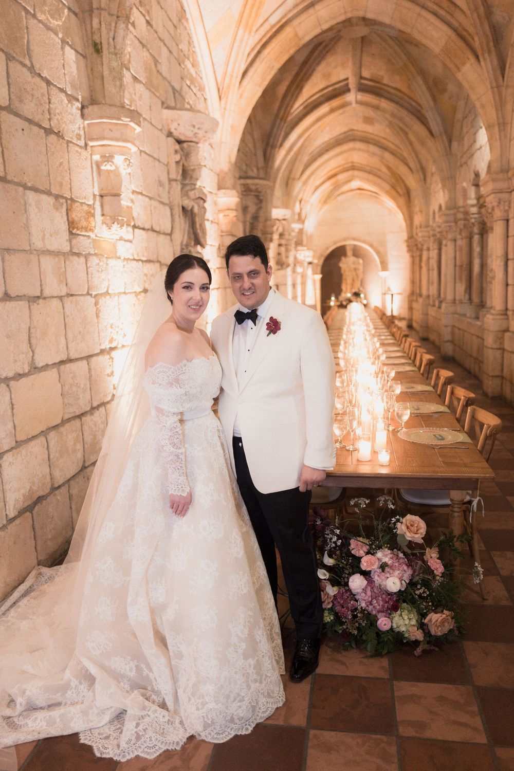 Bride and groom posing in elegant stone archway venue with candlelit reception table and floral arrangements.