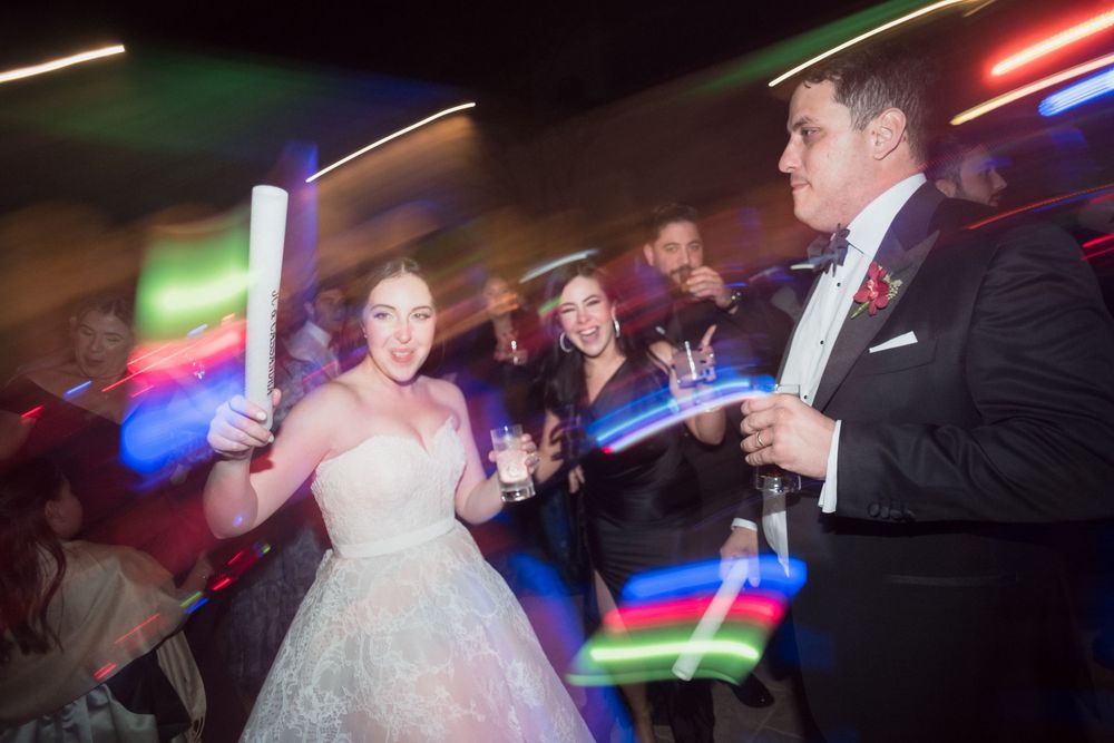 Bride and groom dancing with colorful glow sticks at a vibrant wedding reception party.