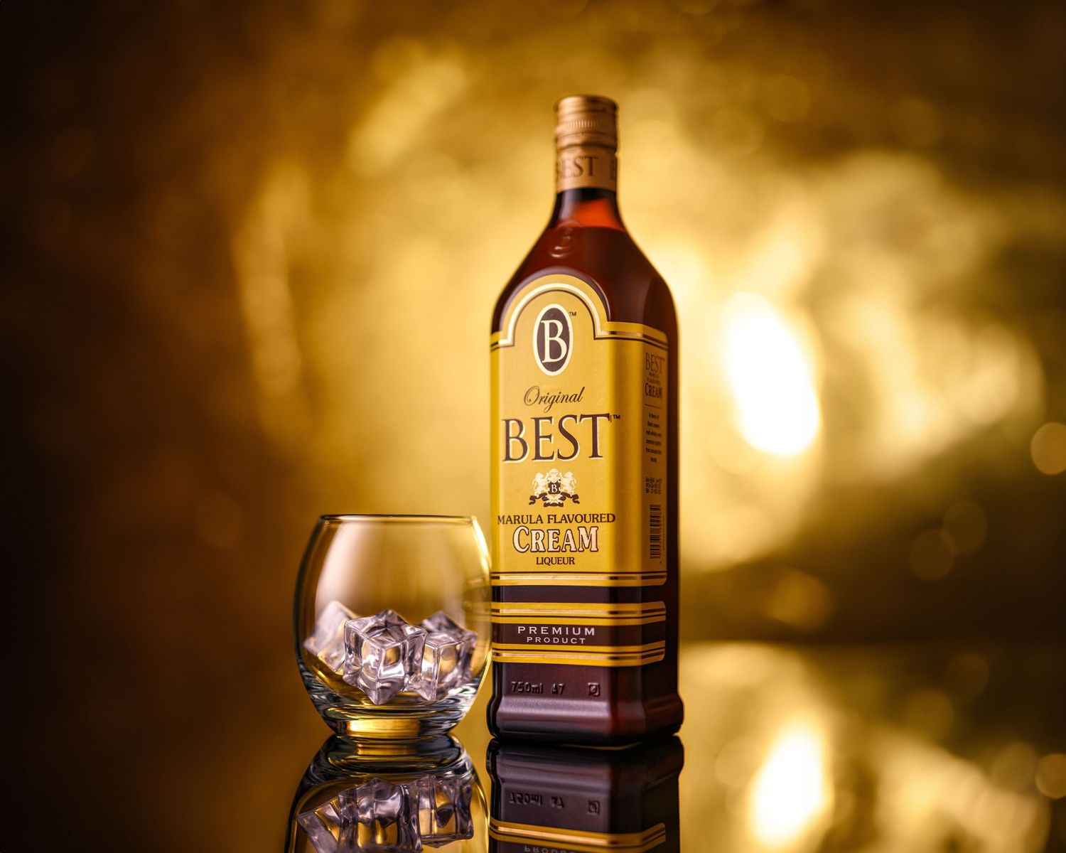 A bottle of Best Original liqueur beside a glass with ice cubes on a reflective surface with a golden bokeh background.