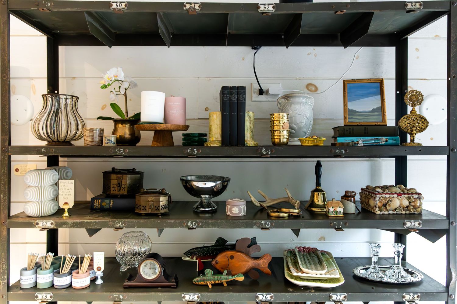 Elegant display shelves featuring decorative vases, framed art, books, clocks, and ornamental fish figurines in a stylish boutique setting.