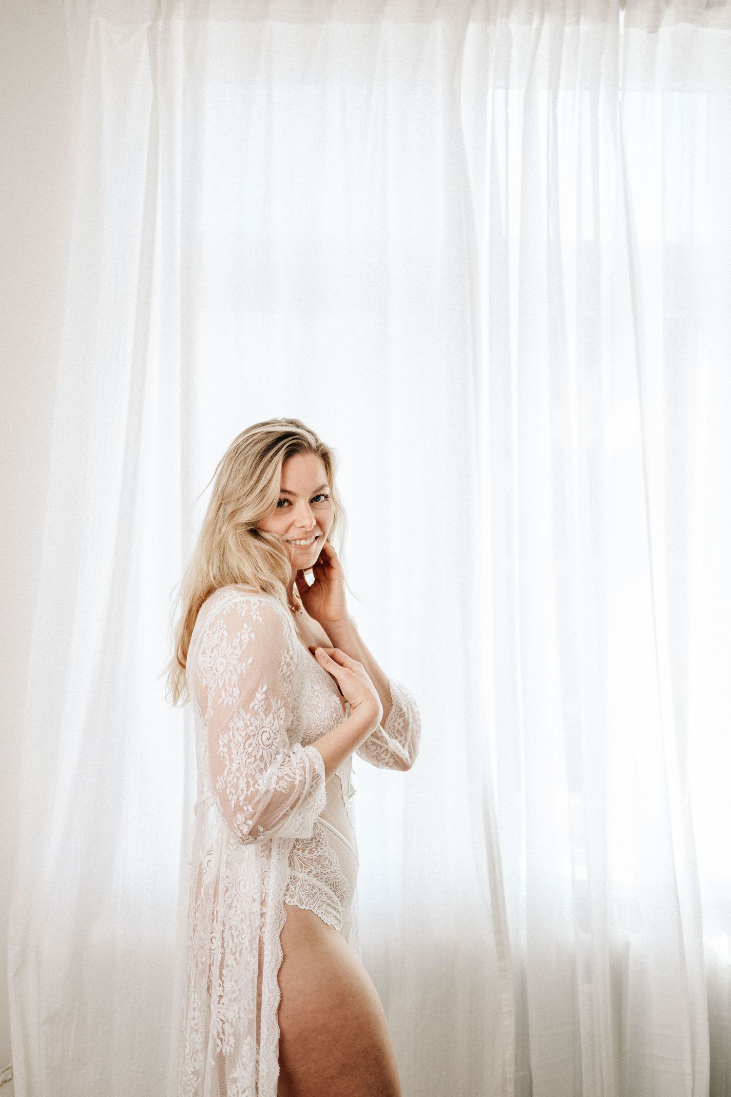 Boudoir Portrait in einer sinnlichen Pose einer Frau mit sanften Fensterlicht vor weißen Vorhängen