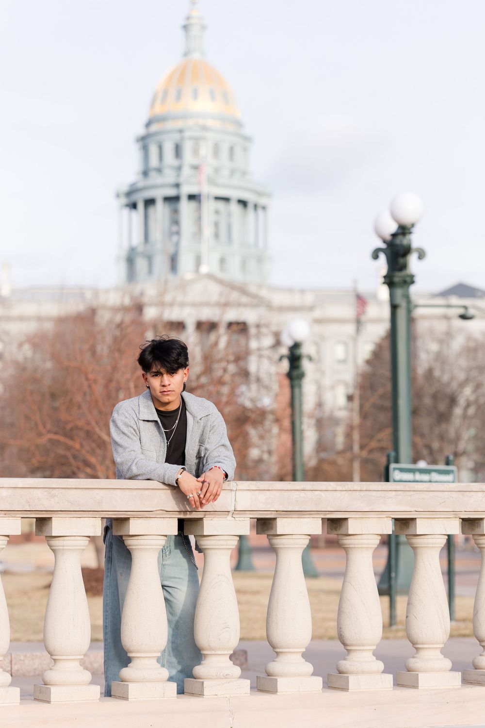 Young man leaning on stone balustrade with Colorado State Capitol gold dome in background.
