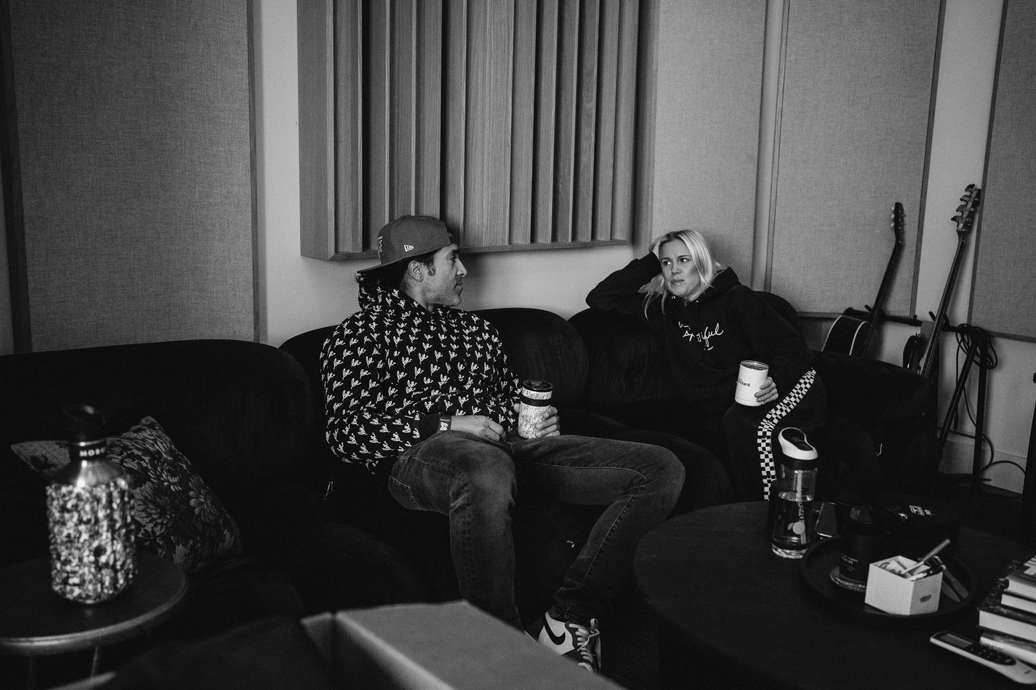 Two people sitting on a dark couch in a music studio, having a conversation in black and white photo.