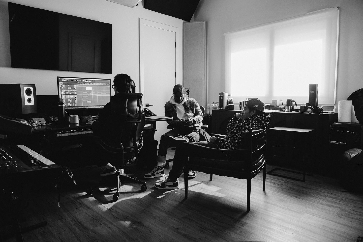 Black and white photo of music producers working in a recording studio with monitors and computer equipment.