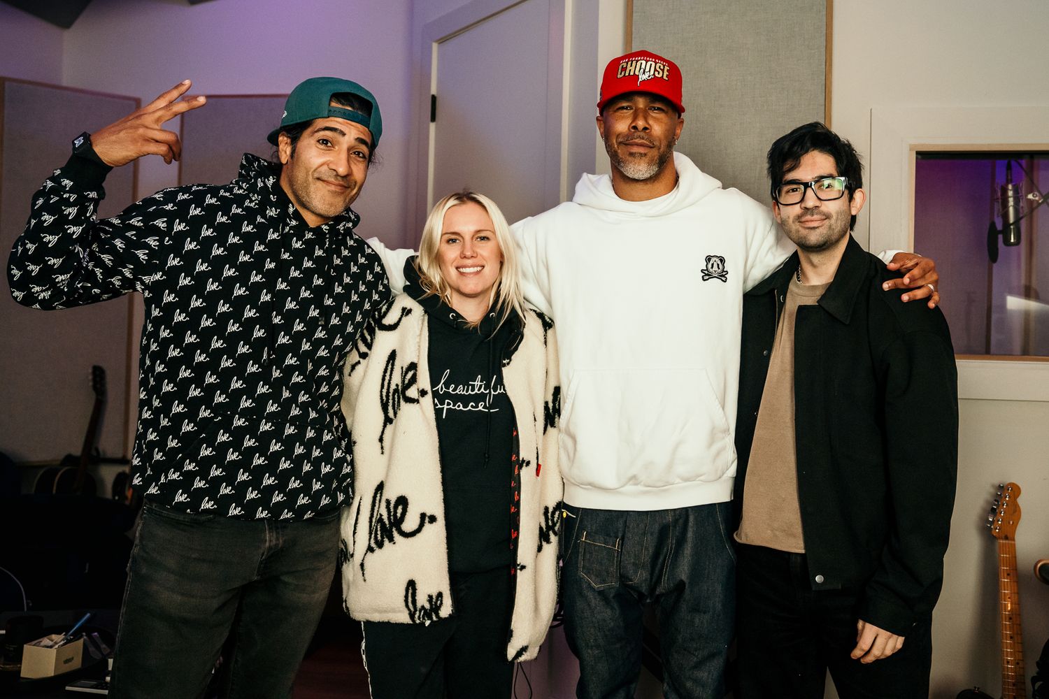 Four people smiling together in a recording studio, posing for a group photo in a casual, creative music environment.