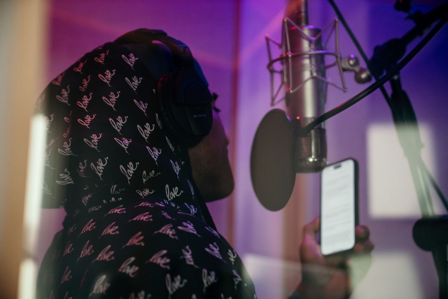 A musician wearing headphones records vocals in a professional studio with a condenser microphone and pop filter.