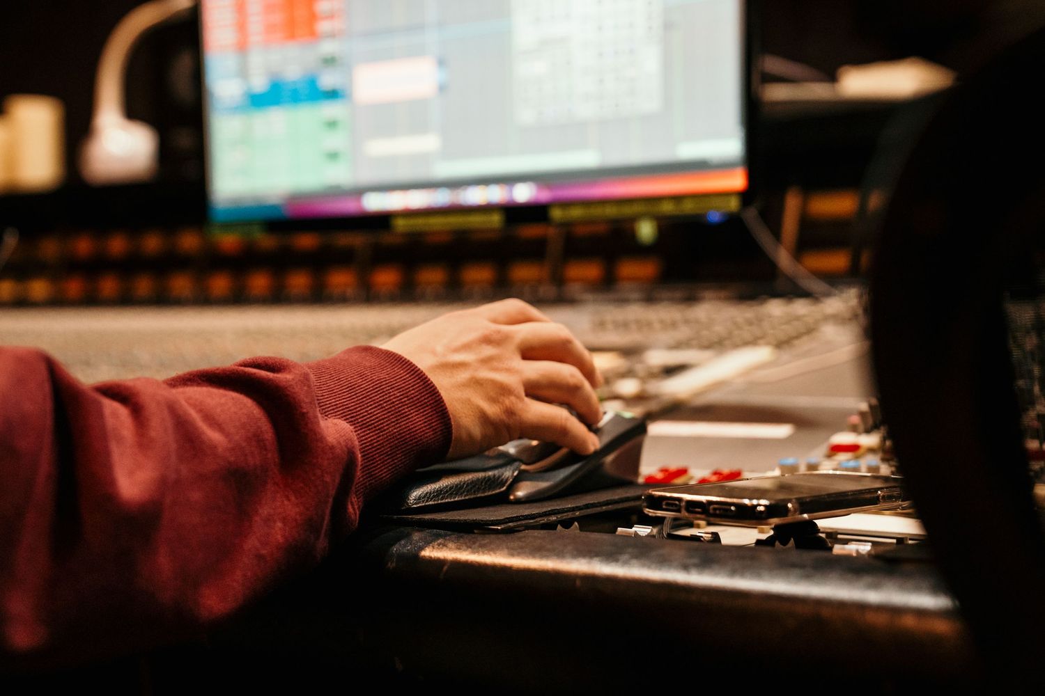 A music producer's hand on a mixing console mouse in a professional recording studio with monitors in background.